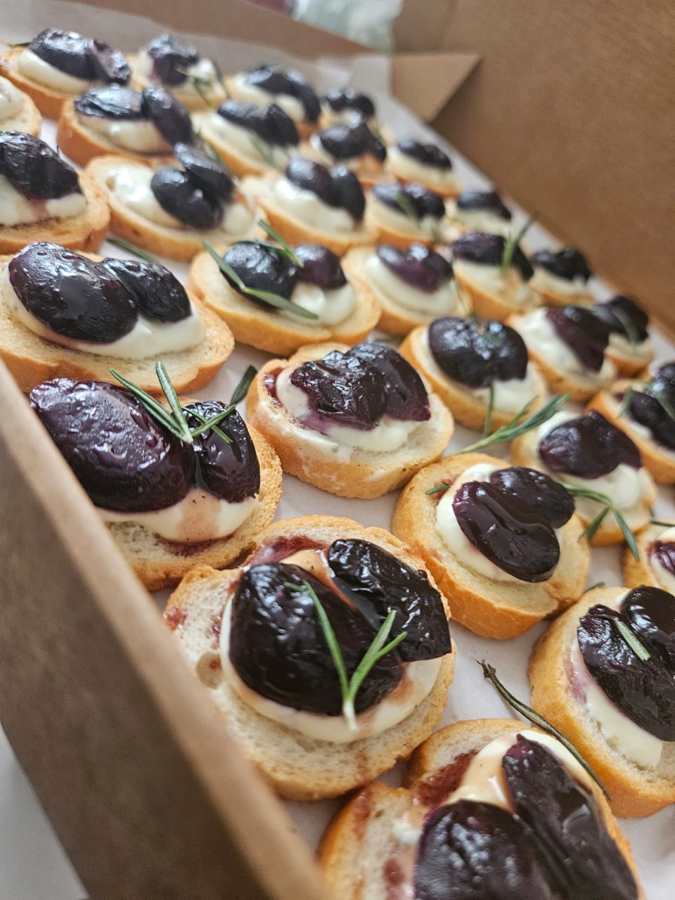 Canapés topped with roasted grapes, cream, and rosemary