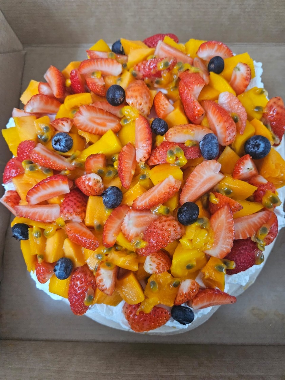 Celebration cake topped with mango, strawberries, blueberries, and passion fruit